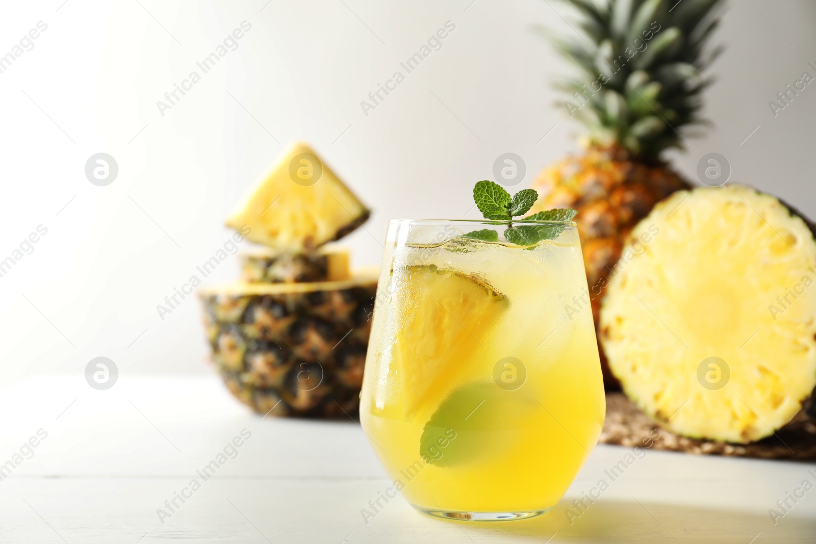 Photo of Tasty pineapple cocktail with mint in glass on light table