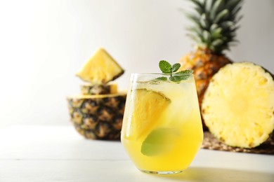 Photo of Tasty pineapple cocktail with mint in glass on light table