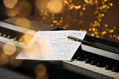 Photo of Sheet with musical notes and pen on piano against blurred lights, closeup. Bokeh effect