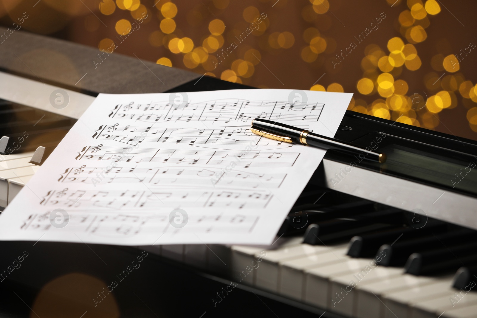 Photo of Sheet with musical notes and pen on piano against blurred lights, closeup. Bokeh effect