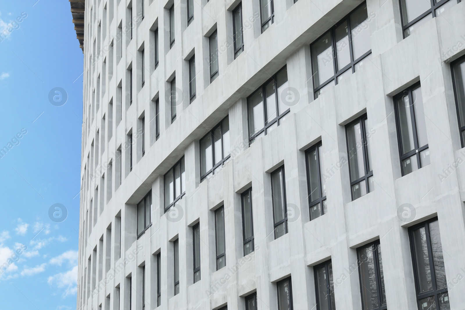 Photo of Modern building with many windows against blue sky, low angle view