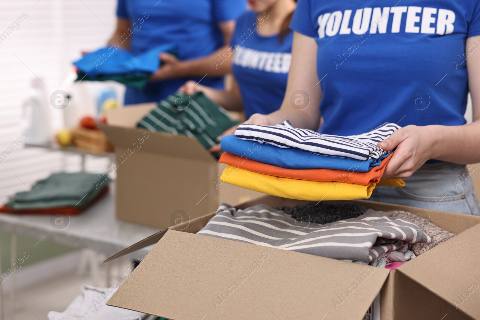 Photo of Volunteers putting clothes into donation boxes at indoors, closeup