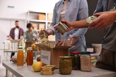 Photo of Volunteers packing food donations at table indoors, closeup