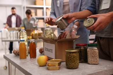 Photo of Volunteers packing food donations at table indoors, closeup