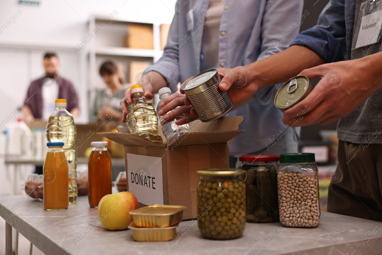 Photo of Volunteers packing food donations at table indoors, closeup