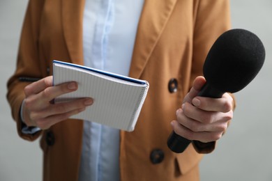 Photo of Journalist with microphone and notebook on grey background, closeup