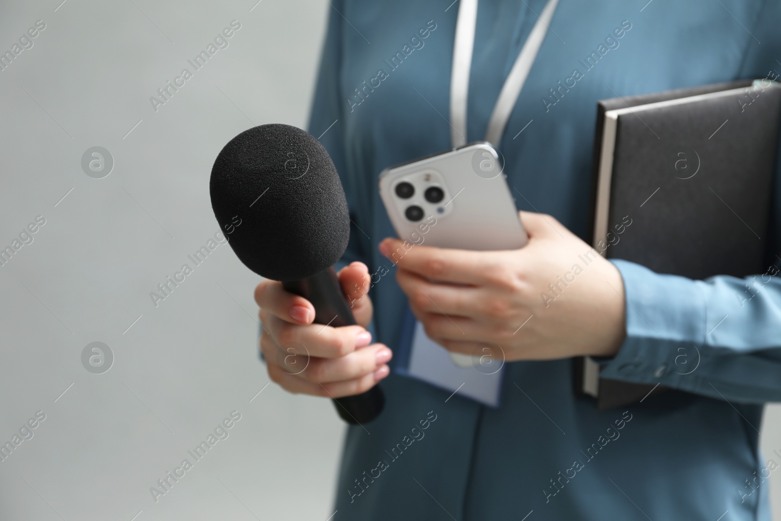 Photo of Journalist with microphone, smartphone and notebook on grey background, closeup. Space for text