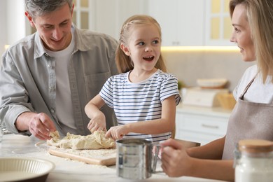 Photo of Happy parents and their daughter making dough at white marble table in kitchen