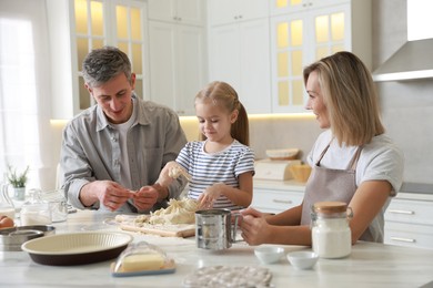 Photo of Happy parents and their daughter making dough at white marble table in kitchen