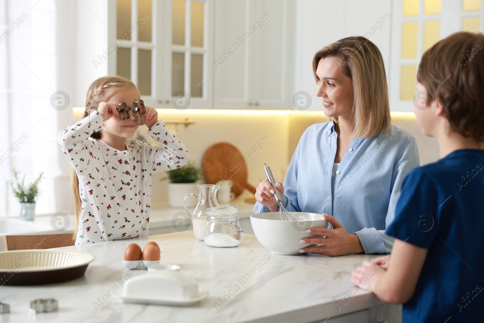 Photo of Mother and her kids making dough at white marble table in kitchen