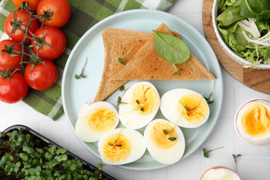 Photo of Cut hard boiled eggs with bread on white tiled table, flat lay