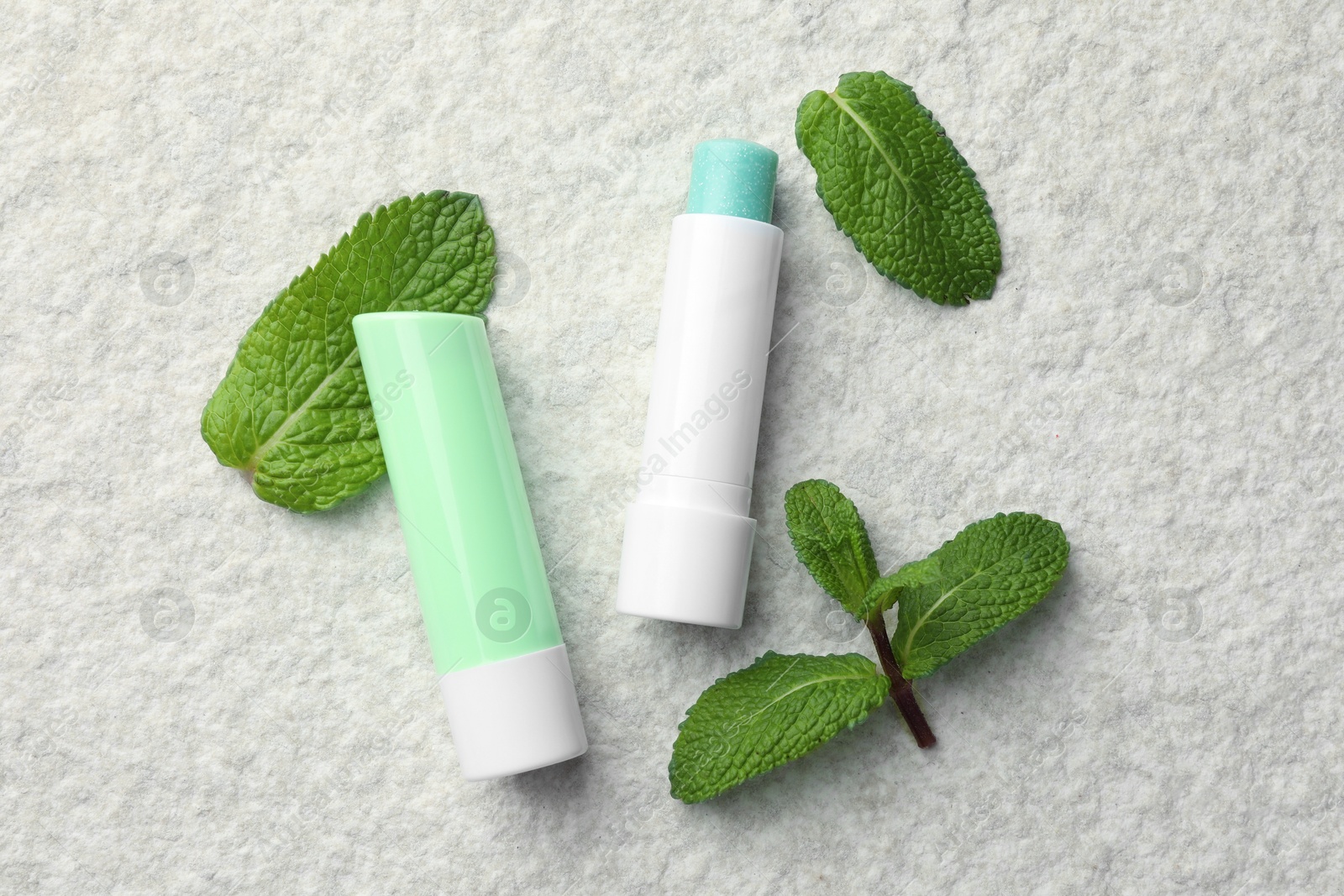 Photo of Mint lip balms and green leaves on beige textured table, flat lay. Cosmetic product