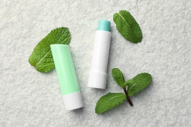 Photo of Mint lip balms and green leaves on beige textured table, flat lay. Cosmetic product