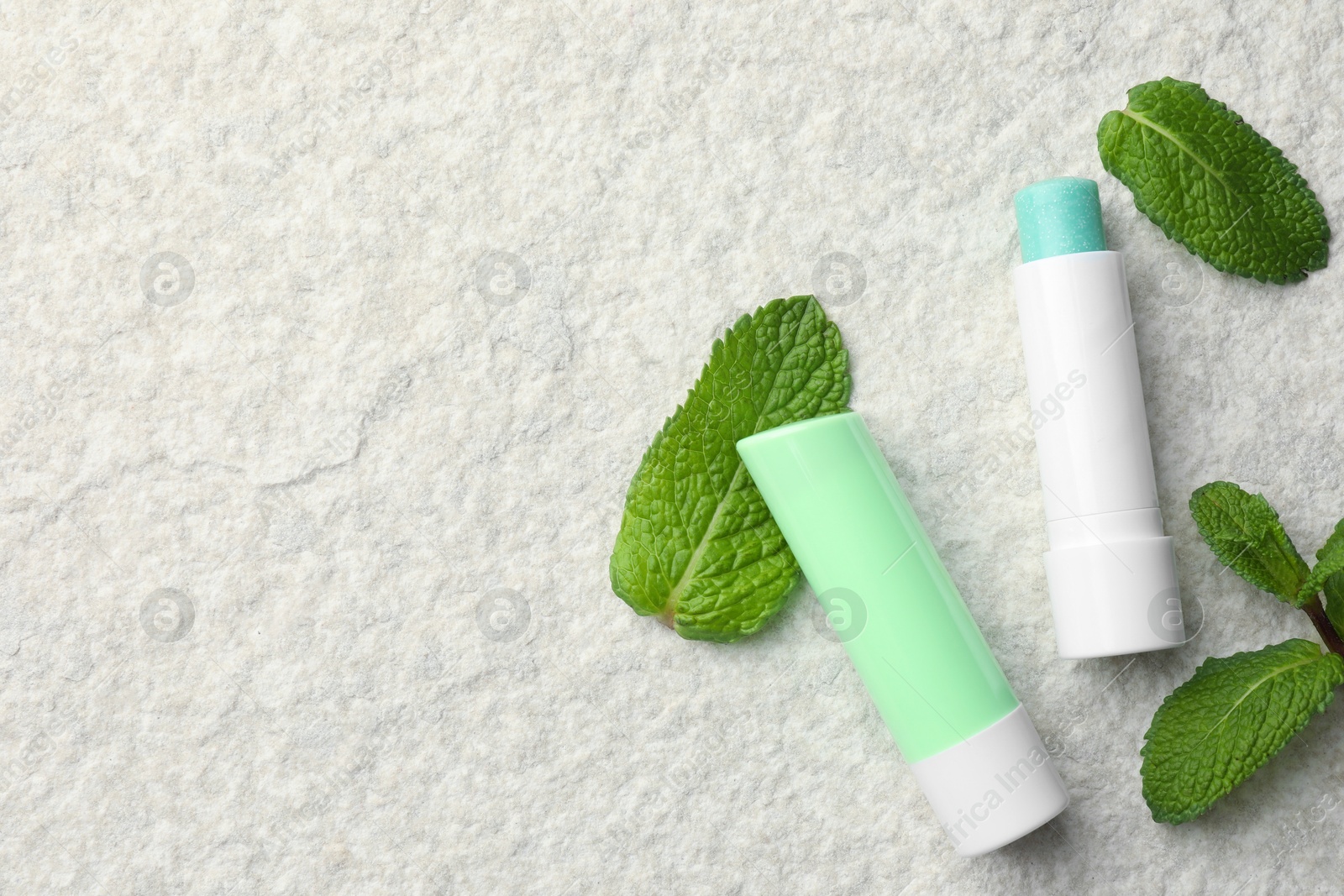 Photo of Mint lip balms and green leaves on beige textured background, flat lay. Space for text