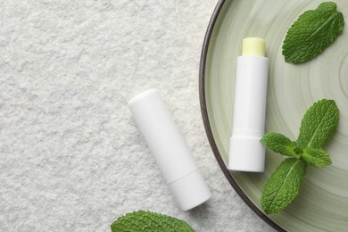 Photo of Mint lip balms and green leaves on beige textured background, top view. Space for text