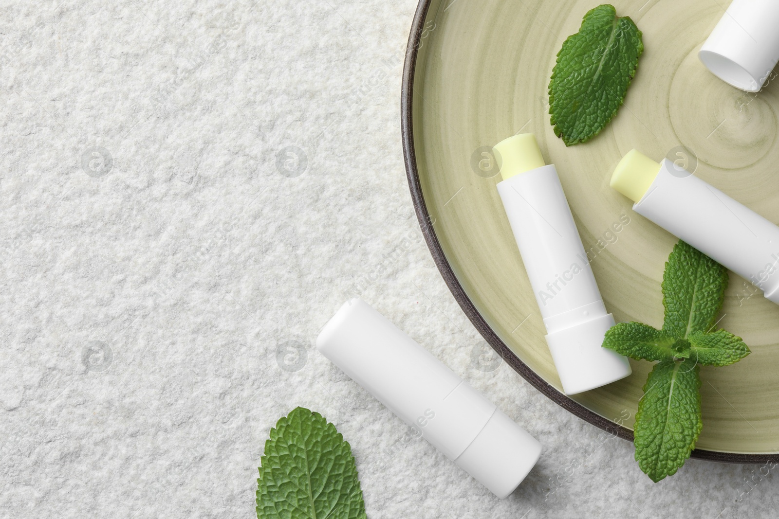 Photo of Mint lip balms and green leaves on beige textured background, top view. Space for text