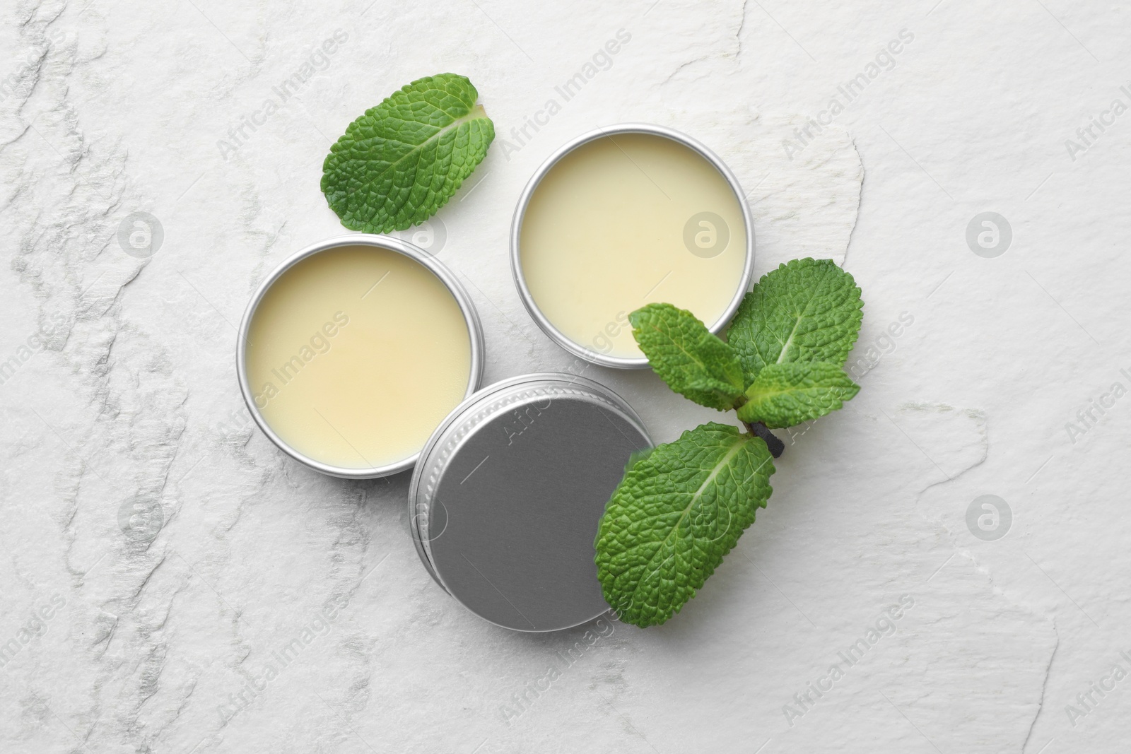 Photo of Mint lip balms and green leaves on beige textured table, flat lay. Cosmetic product