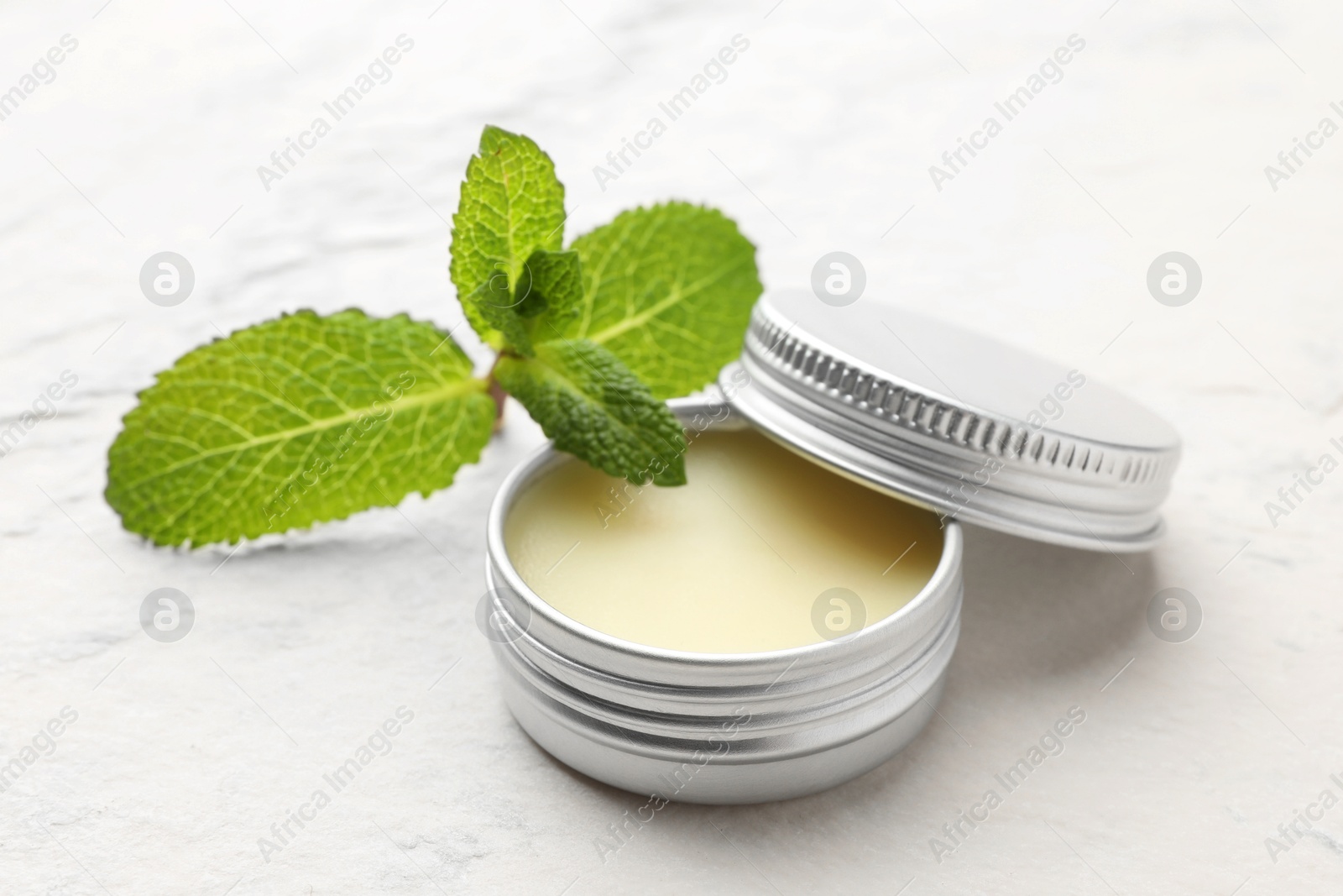 Photo of Mint lip balm and green leaves on beige textured table, closeup. Cosmetic product