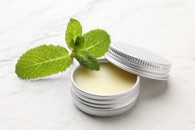 Photo of Mint lip balm and green leaves on beige textured table, closeup. Cosmetic product