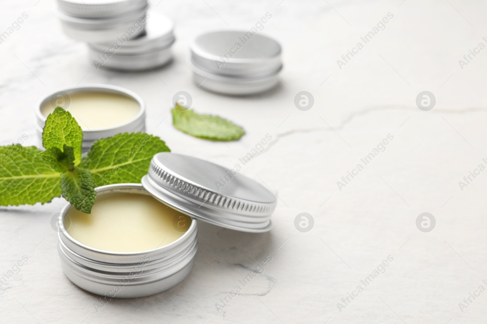 Photo of Mint lip balms and green leaves on beige textured table, closeup. Space for text