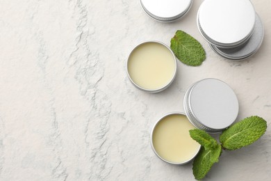 Photo of Mint lip balms and green leaves on beige textured background, flat lay. Space for text