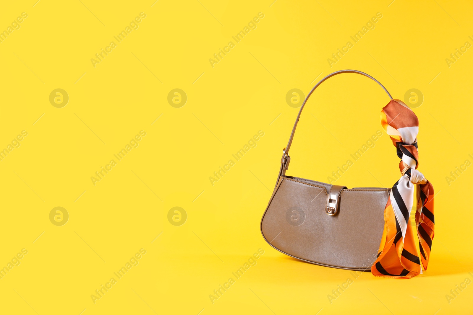 Photo of Stylish brown leather bag with handkerchief on yellow background, space for text