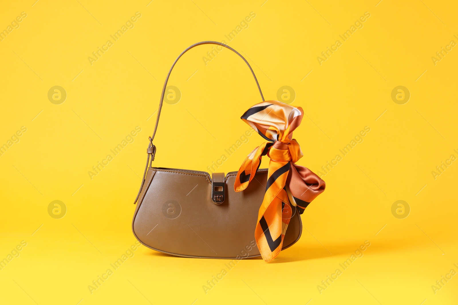 Photo of Stylish brown leather bag with handkerchief on yellow background