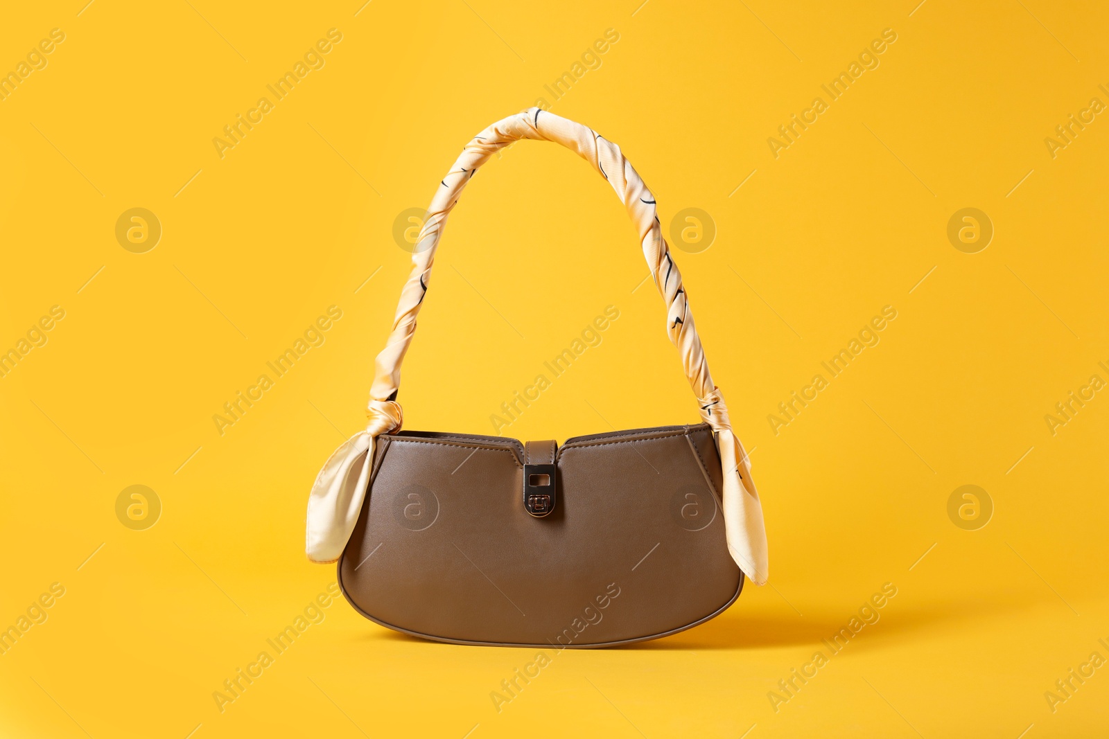 Photo of Stylish brown leather bag with handkerchief on yellow background