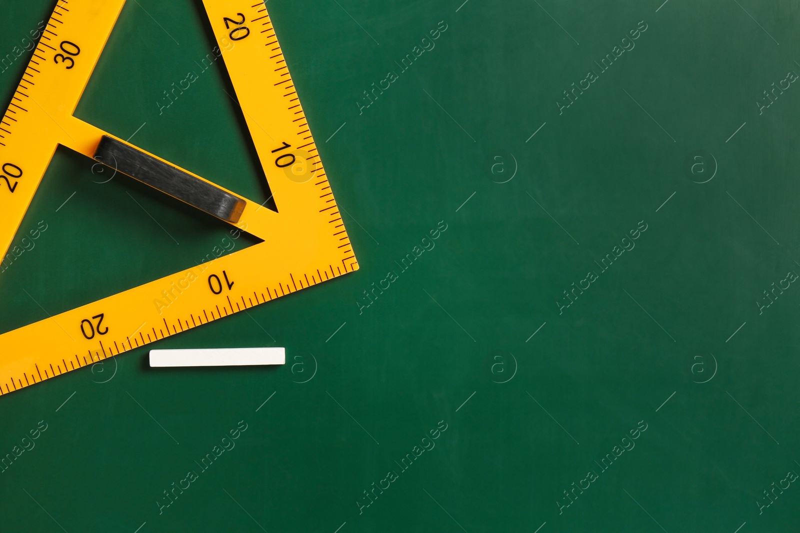 Photo of Triangle ruler and chalk on green chalkboard, top view. Space for text