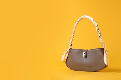 Photo of Stylish brown leather bag with handkerchief on yellow background, space for text