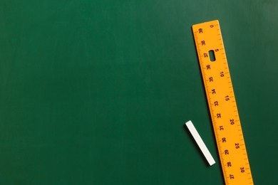 Photo of Ruler and chalk on green chalkboard, top view. Space for text