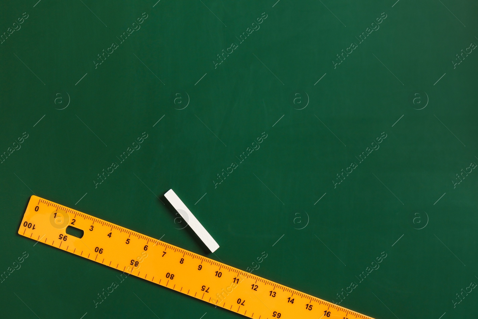 Photo of Ruler and chalk on green chalkboard, top view. Space for text