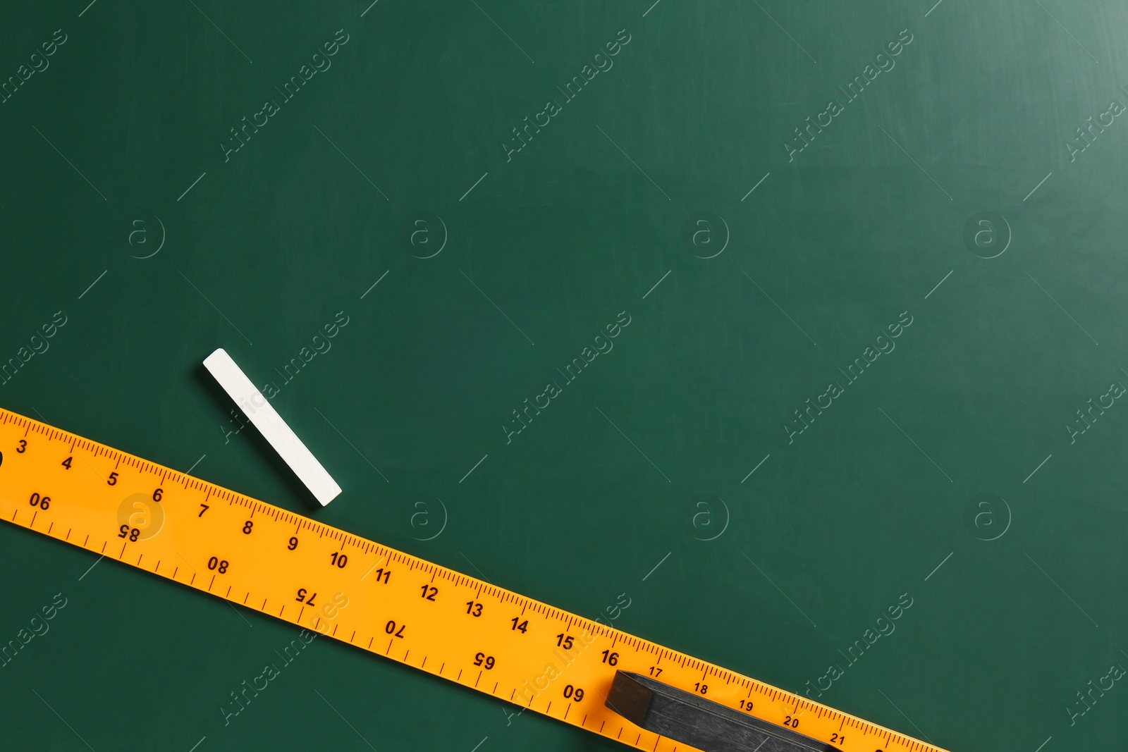 Photo of Ruler and chalk on green chalkboard, top view. Space for text