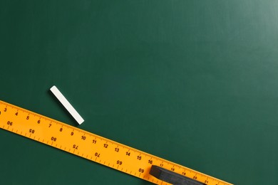 Photo of Ruler and chalk on green chalkboard, top view. Space for text