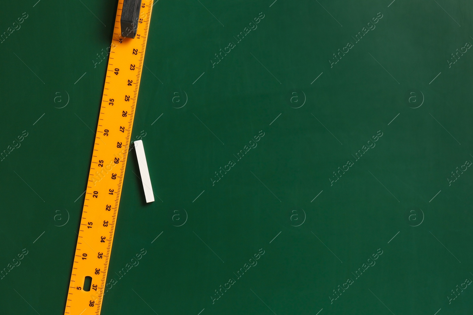 Photo of Ruler and chalk on green chalkboard, top view. Space for text