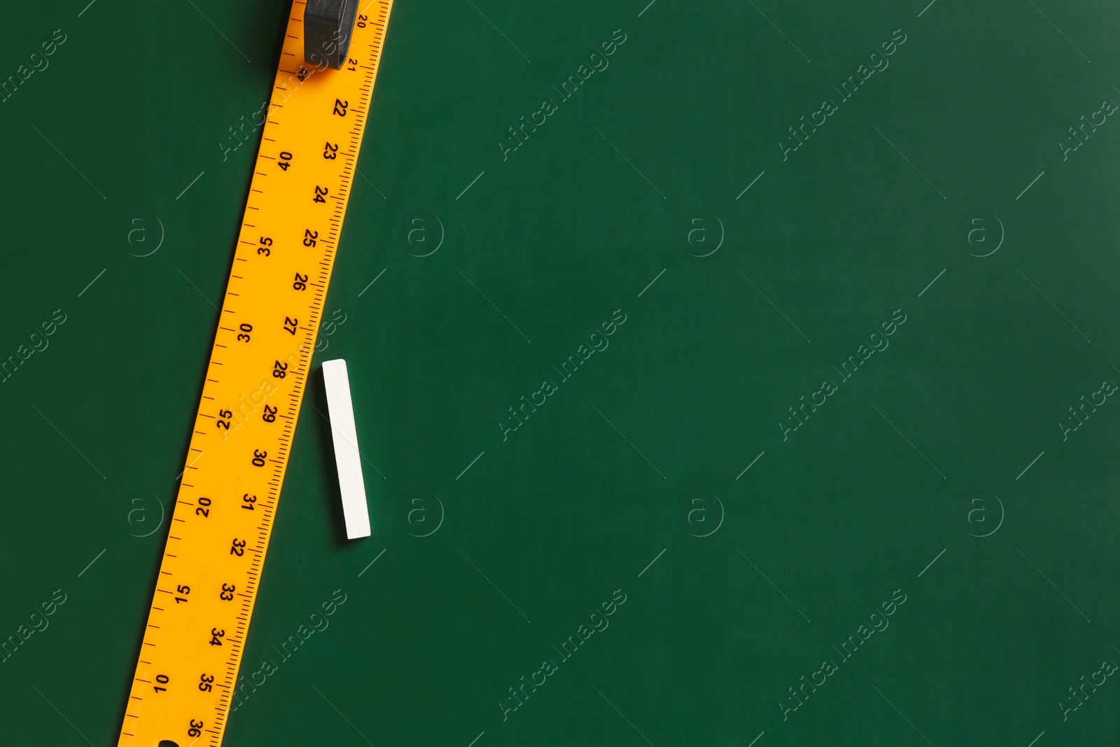 Photo of Ruler and chalk on green chalkboard, top view. Space for text