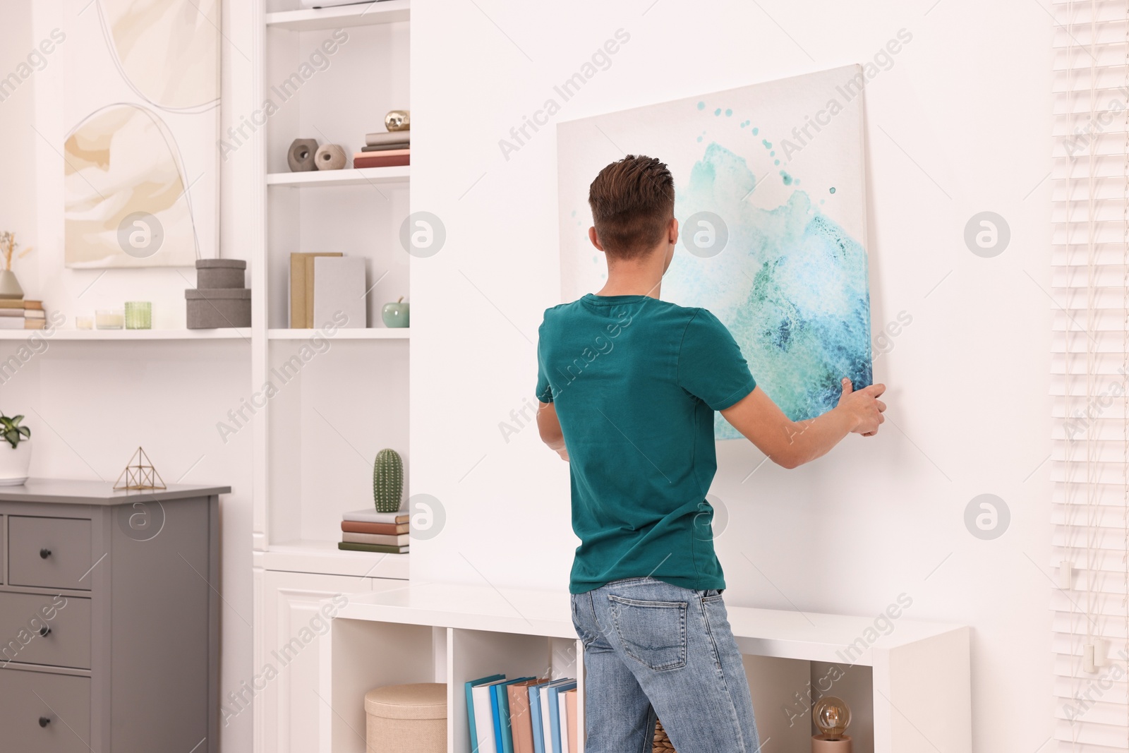 Photo of Decorator hanging abstract picture indoors, back view