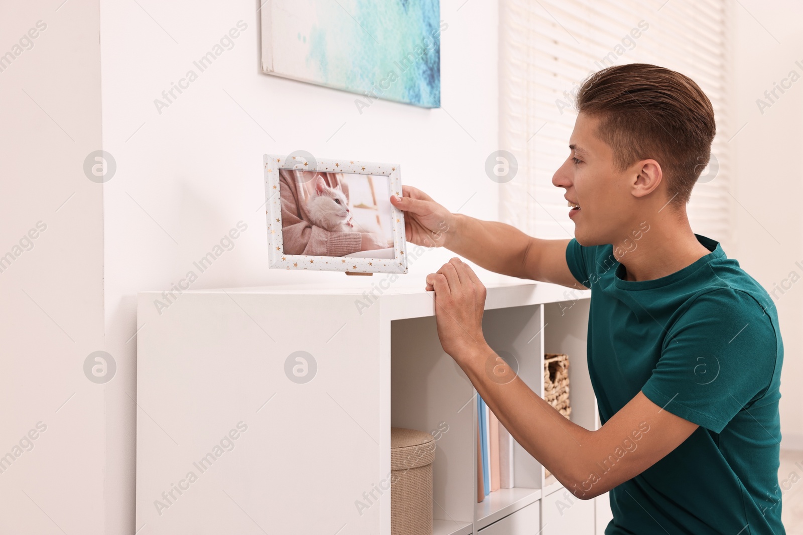 Photo of Smiling young decorator arranging frame with photo indoors