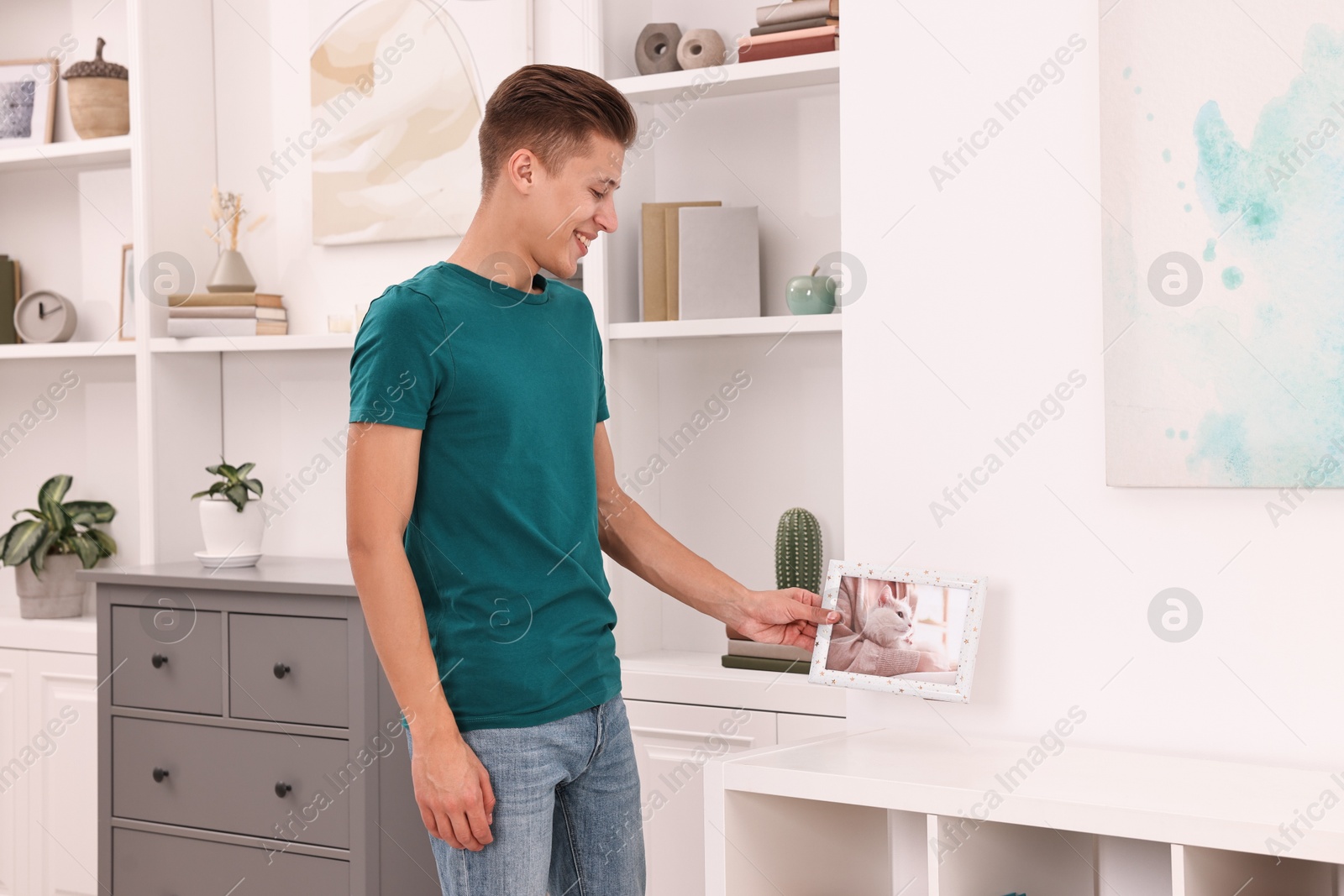 Photo of Smiling young decorator arranging frame with photo indoors