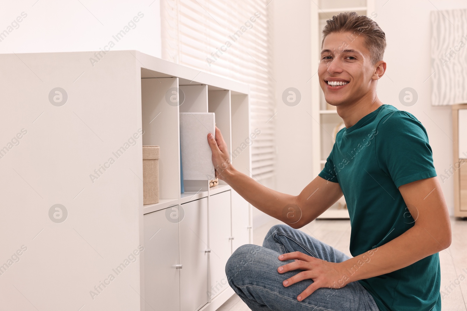 Photo of Smiling decorator arranging books onto shelf indoors