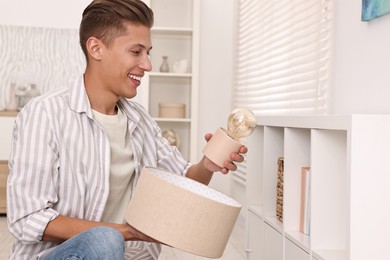 Photo of Smiling decorator arranging nightlight onto shelf indoors