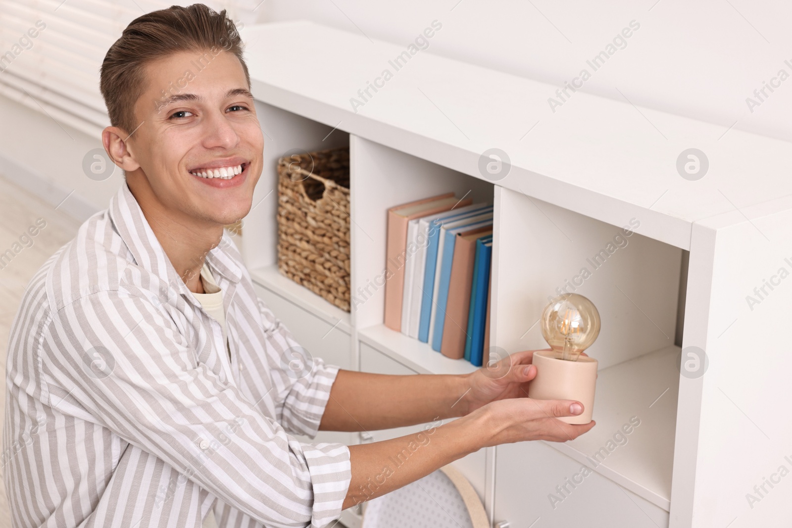 Photo of Smiling decorator arranging nightlight onto shelf indoors