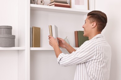 Photo of Smiling decorator arranging books onto shelf indoors