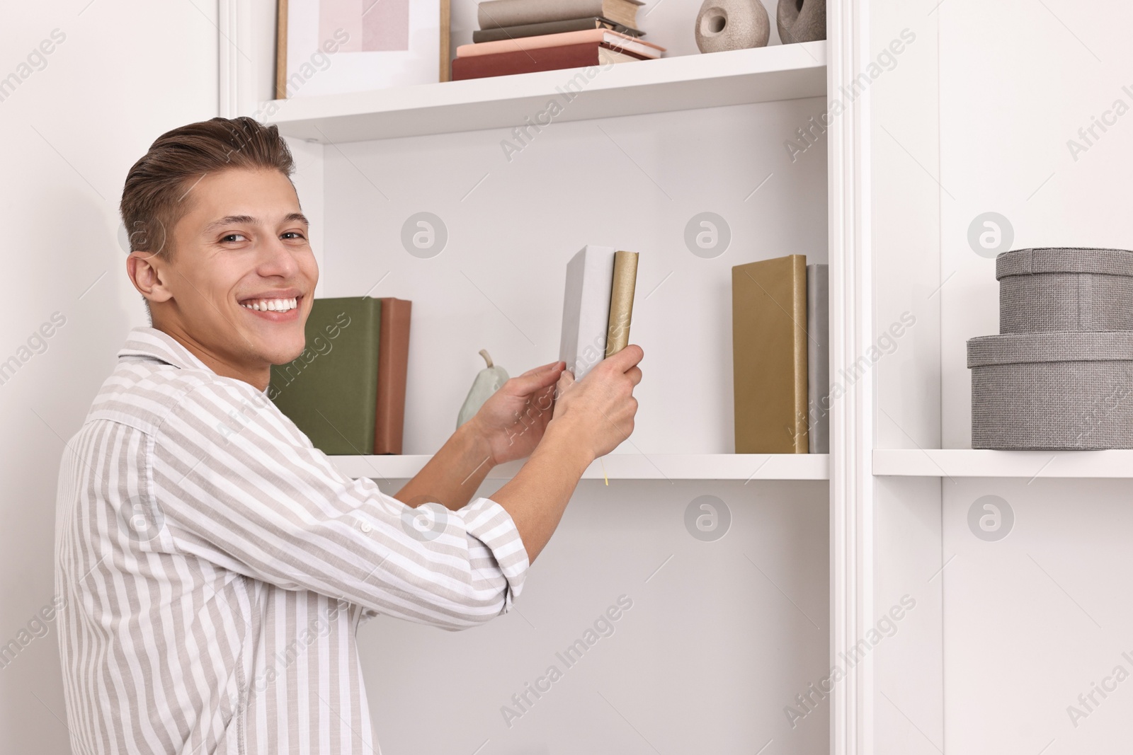 Photo of Smiling decorator arranging books onto shelf indoors