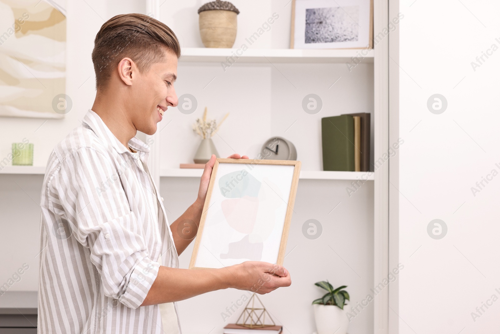 Photo of Smiling decorator with abstract picture near shelving unit indoors