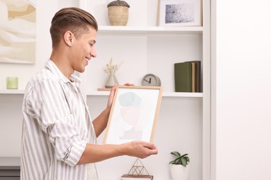 Photo of Smiling decorator with abstract picture near shelving unit indoors