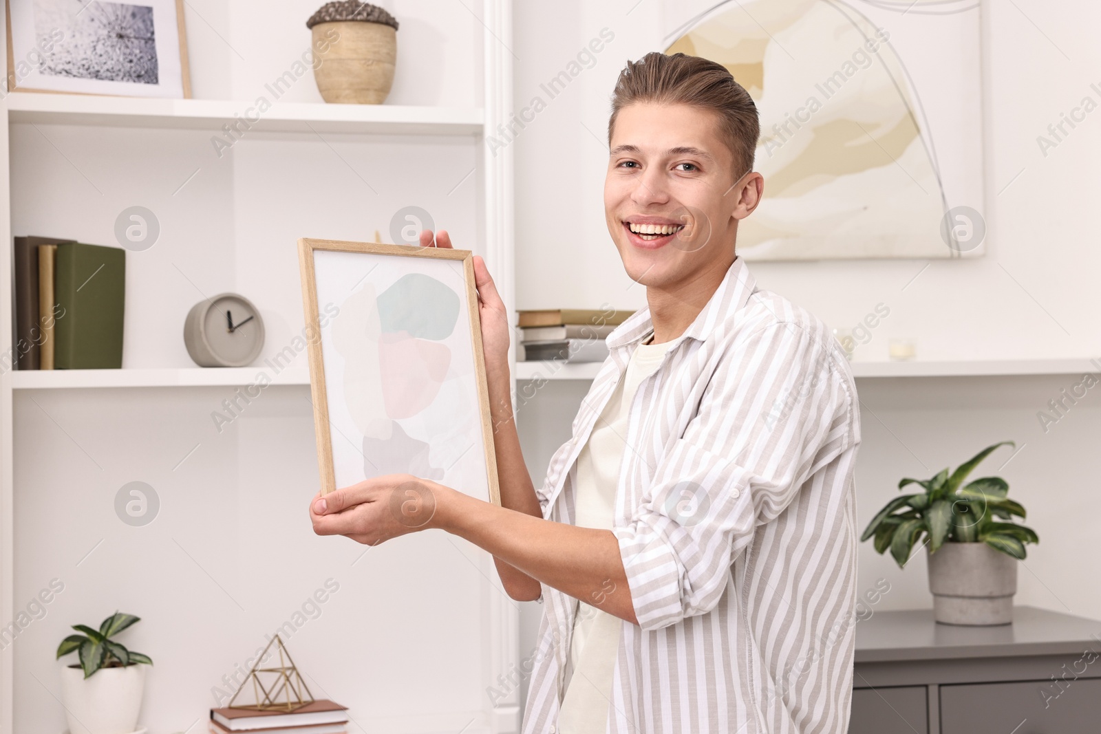 Photo of Smiling decorator with abstract picture near shelving unit indoors