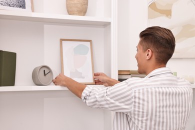 Photo of Male decorator arranging abstract picture onto shelf indoors, back view