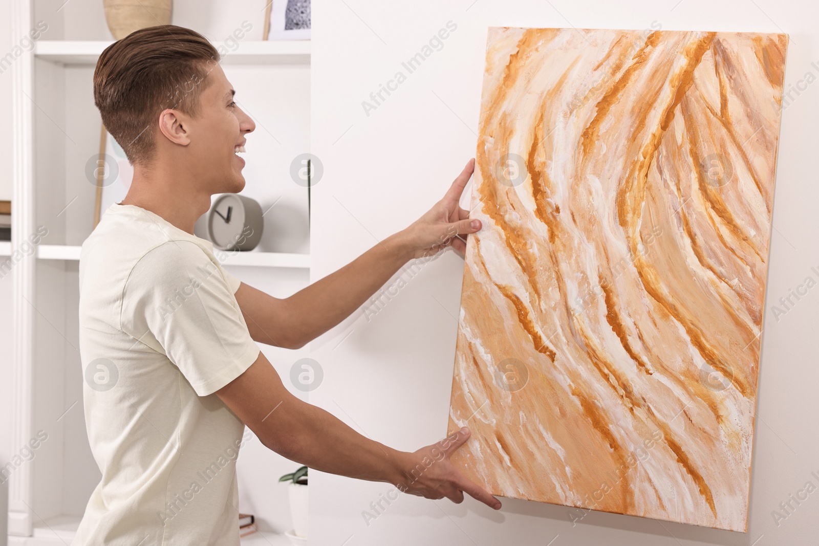 Photo of Smiling young decorator hanging abstract picture indoors