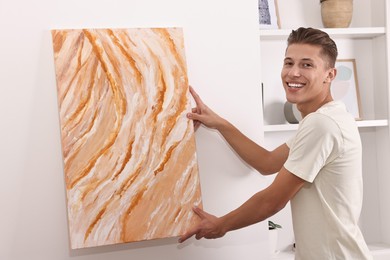 Photo of Smiling young decorator hanging abstract picture indoors